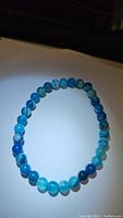 Photo of ocean blue agate round bead stretchy bracelet arranged in circle on white surface with black background.