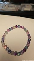 Photo of a round beaded stretchy bracelet made from rainbow fluorite beads displaying multi-color natural hues including purple, green, blue, and pink, laid flat on a white background.