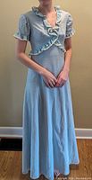 Front view of one light blue vintage 1960s maxi dress with puffed short sleeves and ruffle trim on neckline and sleeves. Floor-length gentle flare skirt seen.