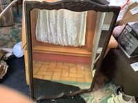 Full view of antique wall mirror resting on floor, showing wood frame, glass surface with reflections and signs of wear.