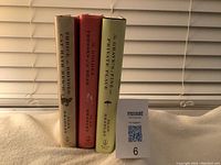 Photo shows three hard cover books by Alan Bradley standing upright on a surface against a white blind background.