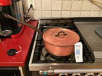 Copper pot with lid seen from above on stove burner, showing overall shape and long handle.