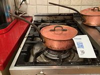 Copper pot with lid and long handle sitting on a stove top.