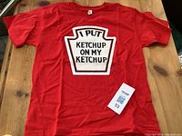 Front view of a red men's large t-shirt with a ketchup-themed graphic in white and black text.