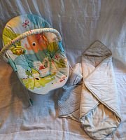 Photo showing baby bouncy chair with colorful animal prints and overhead toy bar, alongside hooded baby blanket with neutral colors.