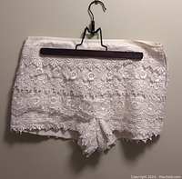 Close-up photo of white lace shorts with scalloped floral lace hem hung on a wooden hanger