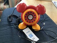 Front view showing Mickey Mouse shaped rotary phone with ears, rotary dial and cables