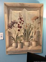First framed print showing potted flowers with a curtain backdrop, four pots in total.