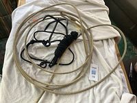 Photo showing cowboy lasso rope and black grappling hook with coiled black rope, placed on a white towel.