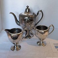 Photo showing silver plated teapot along with matching creamer and sugar bowl with tarnish and scratches.