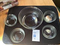 Five glass bowls displayed on black surface; one large round bowl and four smaller round bowls with ribbed vertical fluted design.