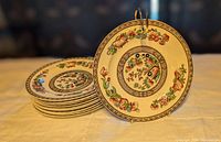 Set of 10 Ye Olde Indian Tree bread and butter plates displayed with one plate on stand and nine stacked underneath, showing detailed floral and fruit pattern with decorative border.