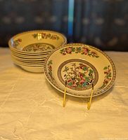Stack of 10 ceramic soup bowls with Ye Olde Indian Tree pattern, showing floral and bird motifs in multiple colors, set on a fabric-covered surface.
