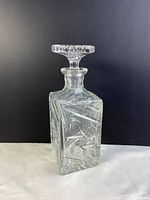 Square crystal decanter featuring detailed pinwheel cut design on a black background.