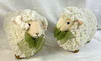 Pair of decorative sheep figurines seen from front angle, showing curly textured wool, green bows, and facial details.