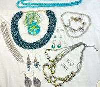 Photo showing various silver tone jewelry items including necklaces, bracelets, and multiple pairs of earrings arranged on a white background.