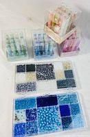Photo showing three glass bead kits in plastic tubes and two rectangular trays with assorted beads in various colors and sizes.