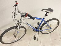 Side angle view of blue and silver Nakamura CB100 men's mountain bike showing frame, tires, and saddle.