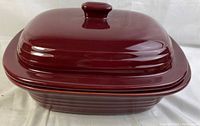 Side and top view of the covered burgundy ceramic baking dish with ribbed design and handle on lid.
