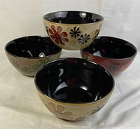 Four Cuisinart ceramic bowls arranged together showing colorful flower patterns on the outside and black glazed interiors.
