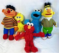 Five Sesame Street plush toys (Ernie, Big Bird, Cookie Monster, Bert, Elmo) displayed on white background