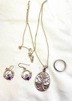 All items laid on white background: oval Tree of Life pendant, non-silver chain, silver band ring, sterling silver earrings with amethyst hearts.