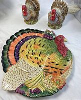 Photo showing the pair of turkey salt and pepper shakers with red heads and multicolored feathers alongside the turkey-shaped decorative plate.