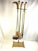 Full view of the four-piece brass fireplace tool set including brush, shovel, poker hanging on the stand with eagle-head handles.