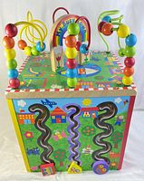 Front view showing colorful wire bead tracks and wooden letter blocks on a vibrant painted wooden cube base.