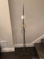 Full view of antique metal lightning rod with pointed tip, glass ball near top, and three-legged metal stand base.
