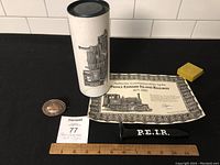 Photo of the two items on display: the Prince Edward Island Railway spike with its white decorative container and certificate, along with a yellow eraser and a ruler for scale.