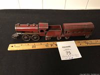 Side view showing entire length of the red metal toy train including engine, cargo car, and passenger car with a measuring ruler below showing 13.5 inches.
