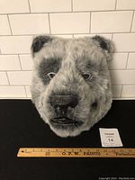 Front view of gray and black faux fur bear mask with detailed face, placed next to a ruler showing about 12 inches tall and 14 inches wide.