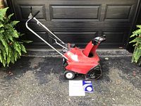 Front side angle of the red Honda HS35 snowblower showing overall condition and included manuals on the ground.