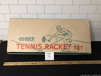 Original closed cardboard box with Jelinek branding, tennis player illustration and title 'Tennis Racket Set'. Ruler placed nearby for size reference.