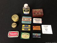 Top-down photo showing all 11 vintage medicine containers including tins and boxes with clear labels such as Ex-Lax, Gin Pills, and Phillips' Tablets.