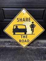 Full front view of the yellow diamond-shaped traffic sign with 'SHARE THE ROAD' text and car and cyclist icons.