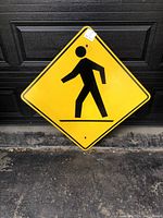 Front side view of the large yellow pedestrians road sign with black silhouette of a walking person, showing color and print condition.