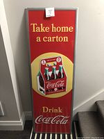 Full vertical view of tin embossed Coca-Cola sign, showing complete text and central carton graphic.