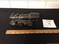 Side view of the black metal locomotive with ruler showing about 7 inches length on a black surface.