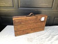 Front view of rectangular wooden carry case with handle, showing natural wood planks and grain.