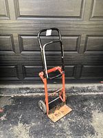 Front view of the wheeled hand truck cart showing the black upper frame and red lower frame with two wheels and a rusted load plate.