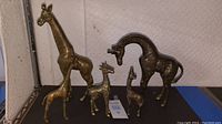 Five brass giraffe figurines displayed on a shelf with different heights and etched surface detailing.