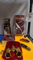 Overall lot showing Winchester knife set in gift tin with three knives and packaging, La Scala opera glasses on red velvet pouch with packaging, and two other small knives in plastic and tin cases.