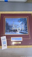 Framed print showing Thomas Kinkade's "Evening Carolers" with snow-covered house, carolers, and warm glowing windows.
