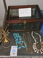 Wood framed glass jewelry box with note explaining details, and elephant-shaped brass jewelry stand with assorted jewelry pieces including turquoise bead necklace, gold chains, and shell necklace.