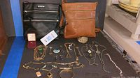 Photo of two Estalon crossbody bags in black and brown with assorted jewelry laid out in front.