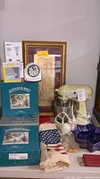 Photo of entire lot including mixer, boxed dishware, framed artwork, bowl, bag, and small items