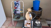 View of wagon, carved wooden statue, black metal pot, blue rolled mat, metal tray, silver bowl, crochet needles, carving kit, walking cane, and assorted small items on a table.