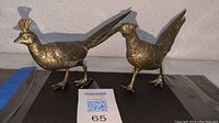 Pair of silver plated pheasant bird figurines placed side by side on a flat surface with lot label in front.